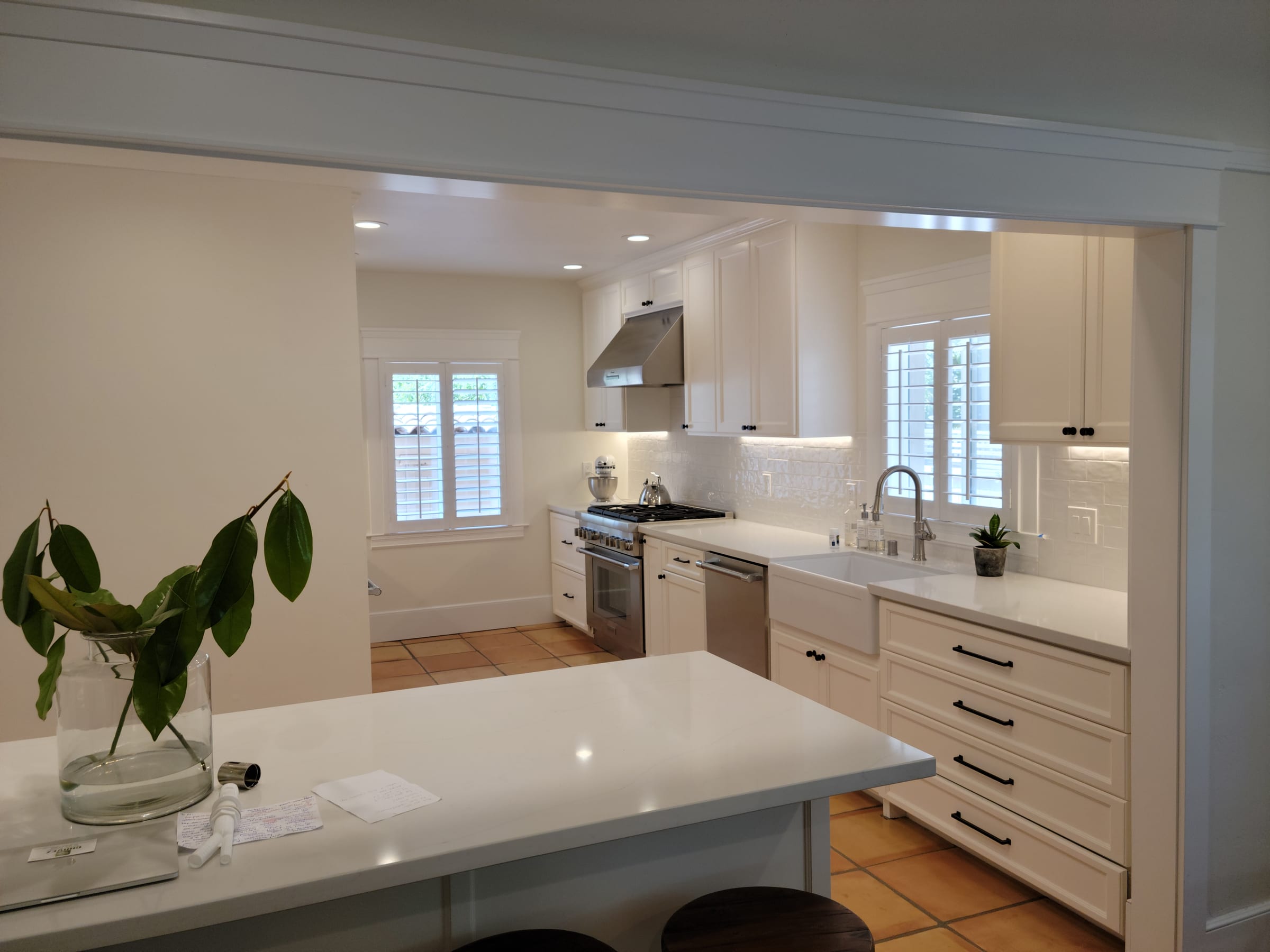 White kitchen with farmhouse sink, black hardware, and terracotta tile flooring