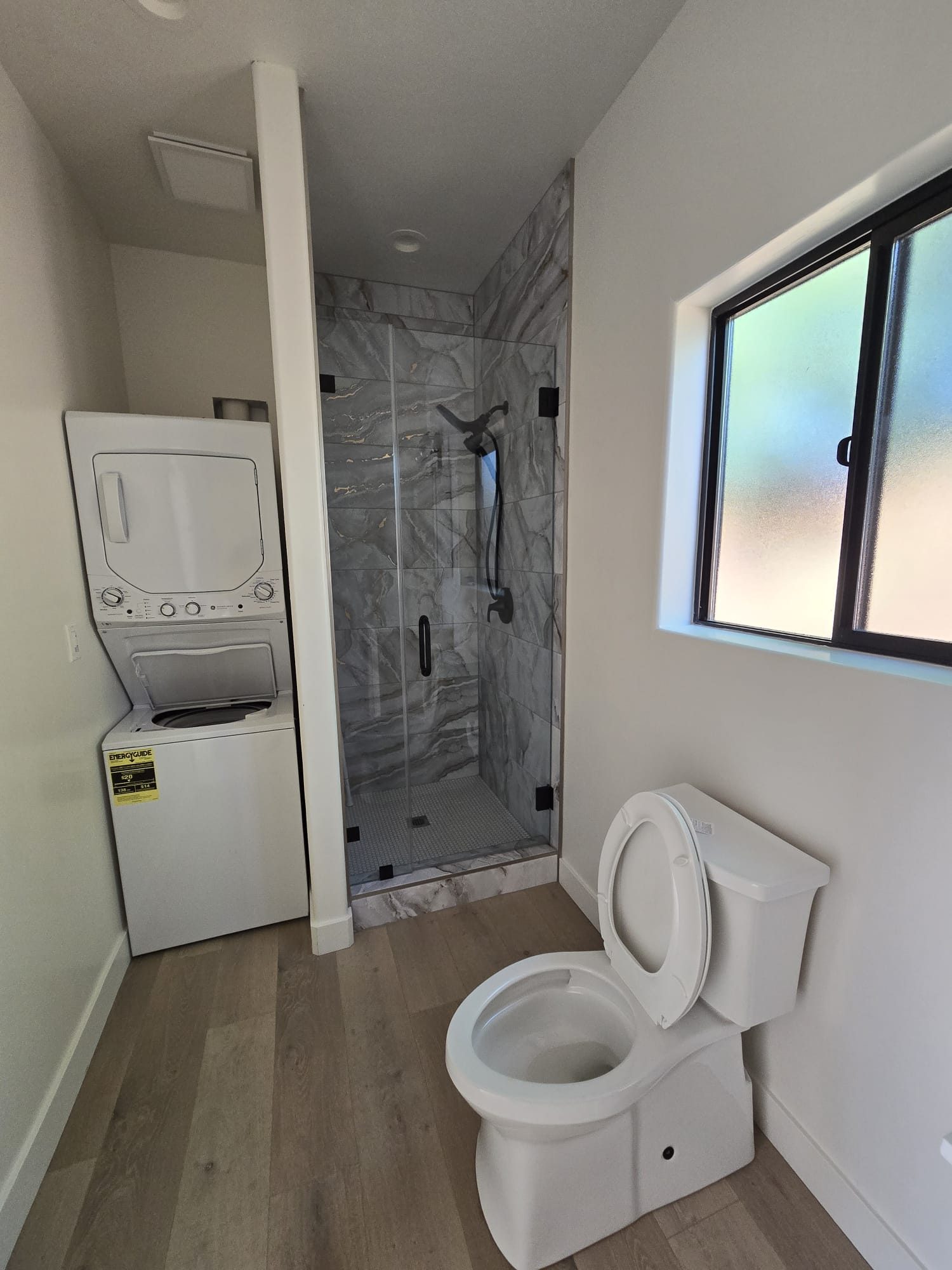ADU bathroom with stacked washer/dryer and marble-tiled shower