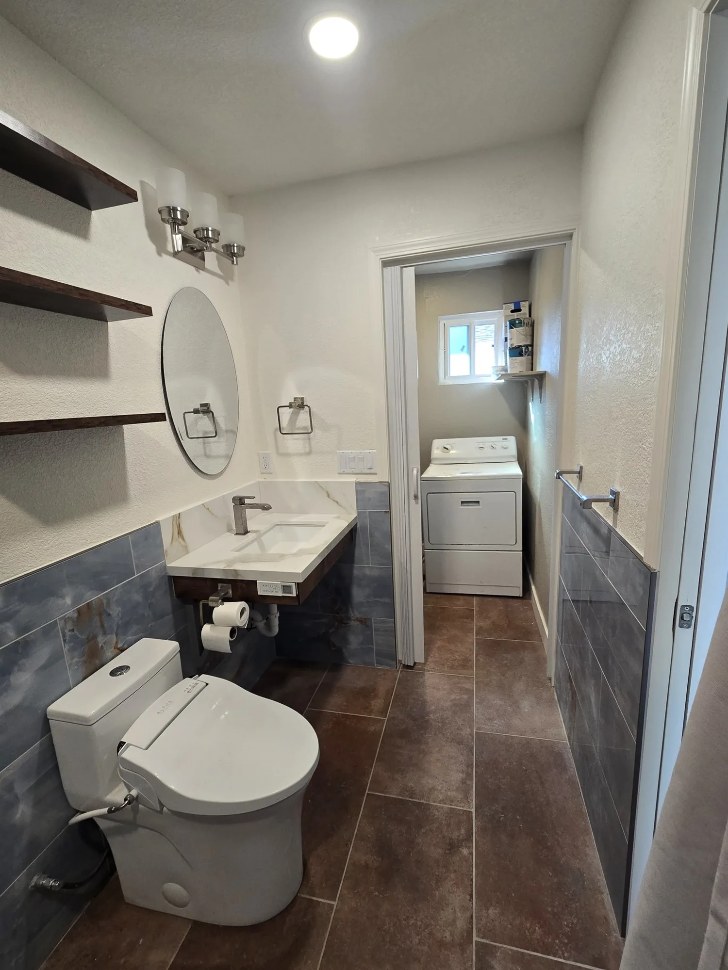 Vanity wall with floating shelves, round mirror and blue tile wainscot