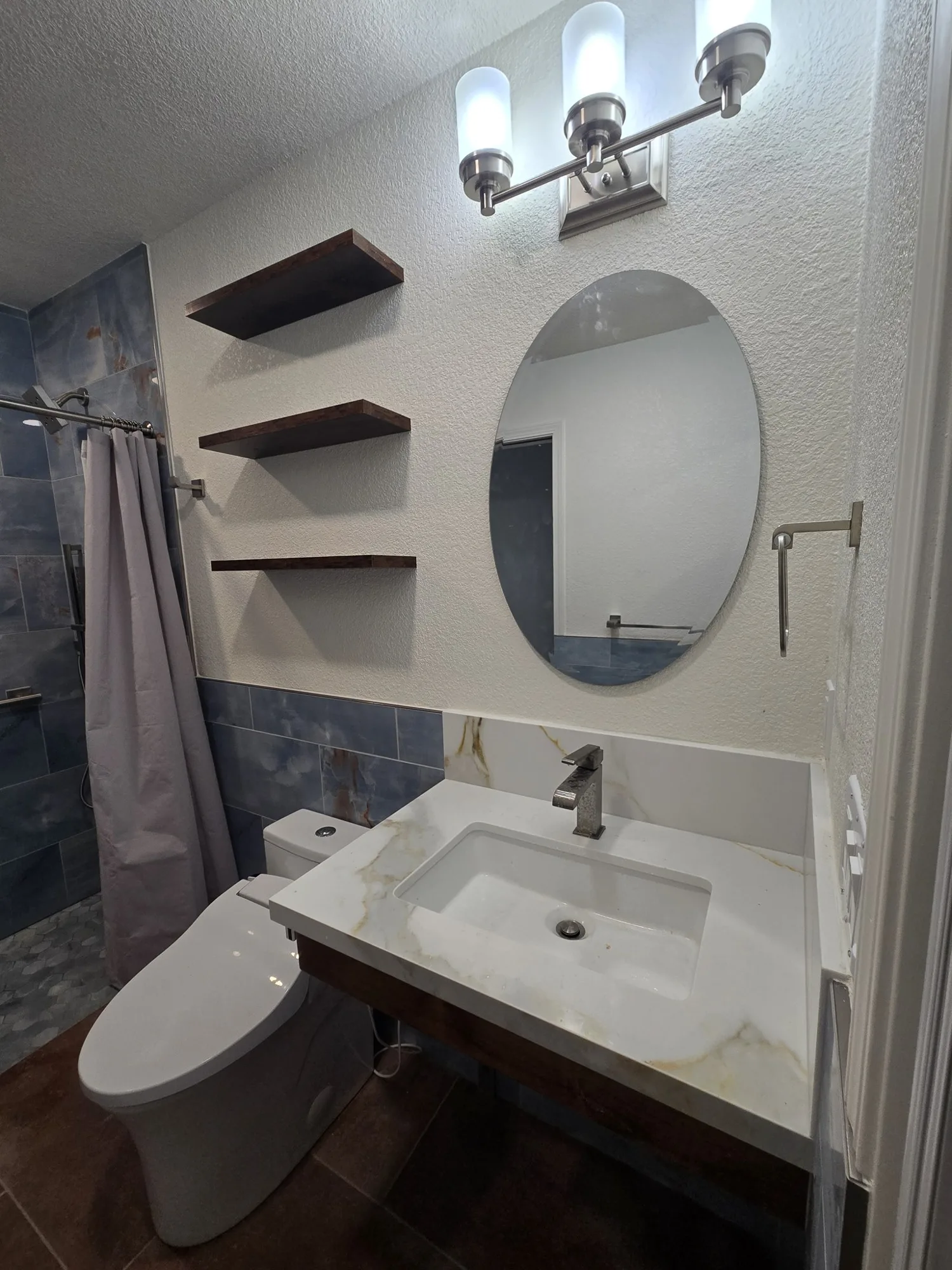 Floating sink with oval mirror and three-light vanity fixture