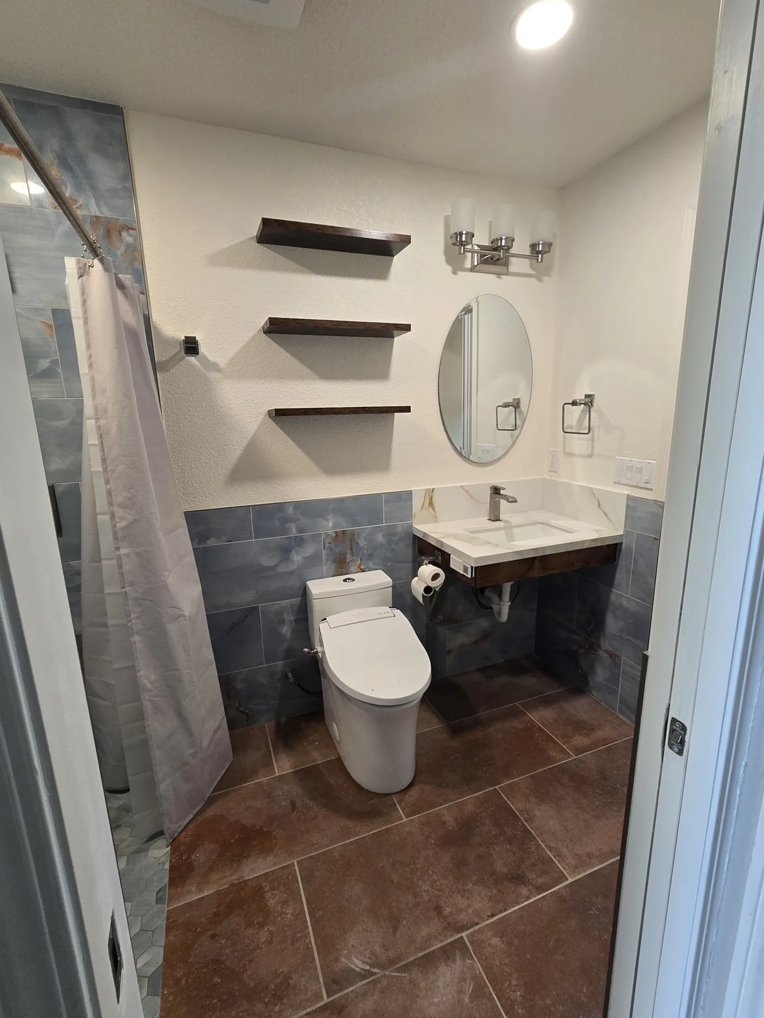 Bathroom entry view showing the curbless shower, vanity and shelving