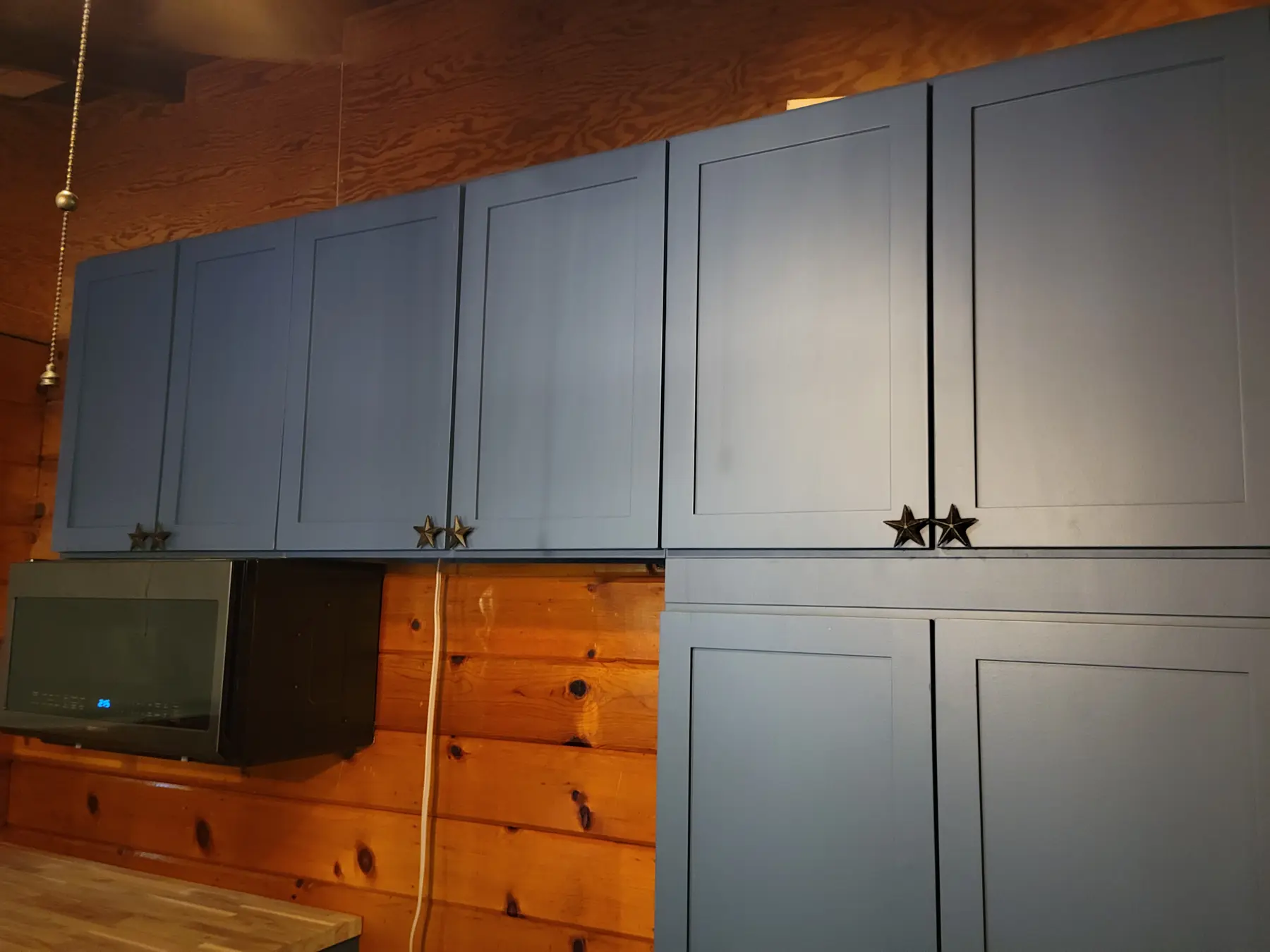Finished cabin kitchen with blue cabinetry set into natural wood walls