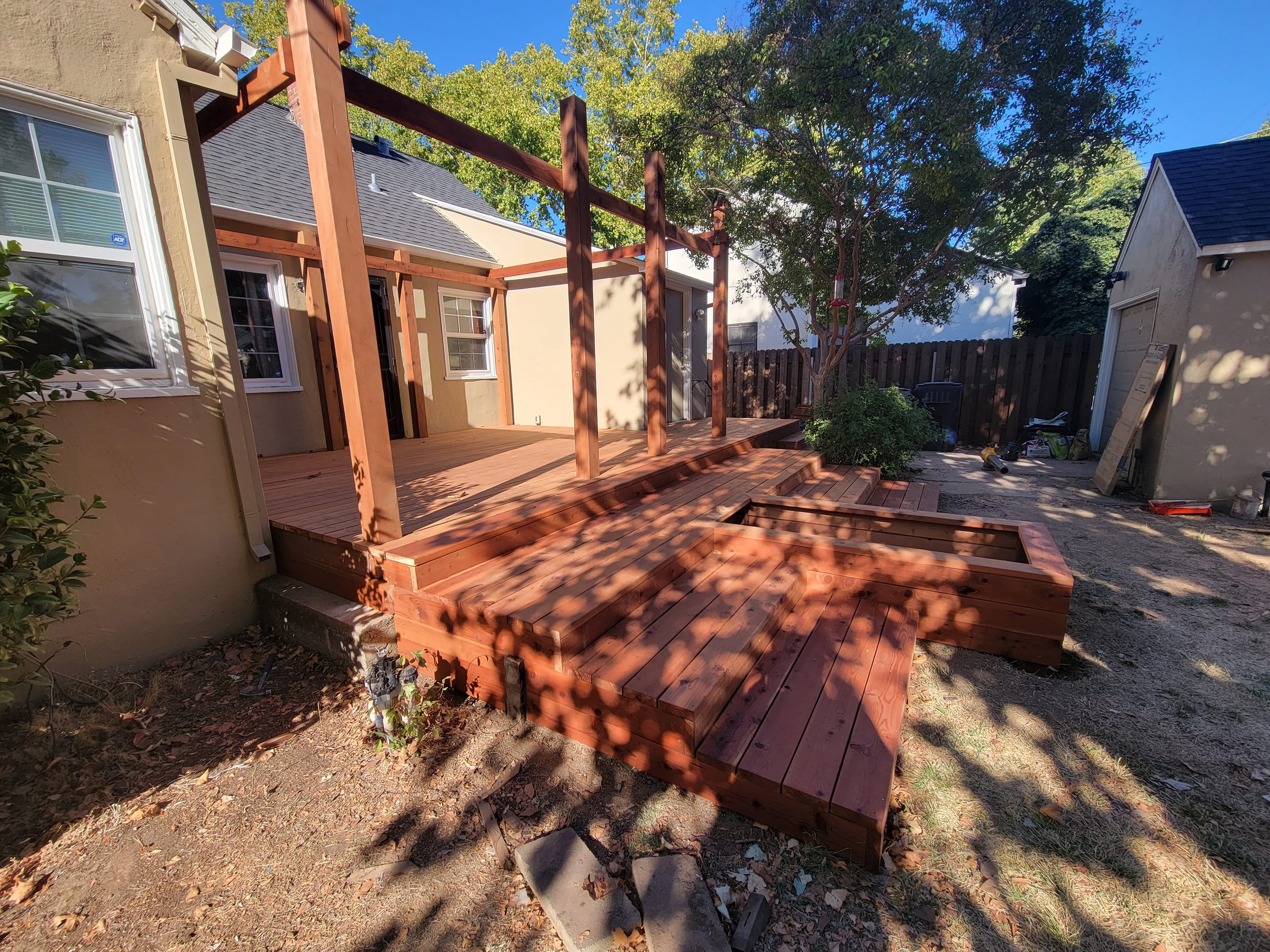 Wood deck with steps and pergola posts behind a stucco home