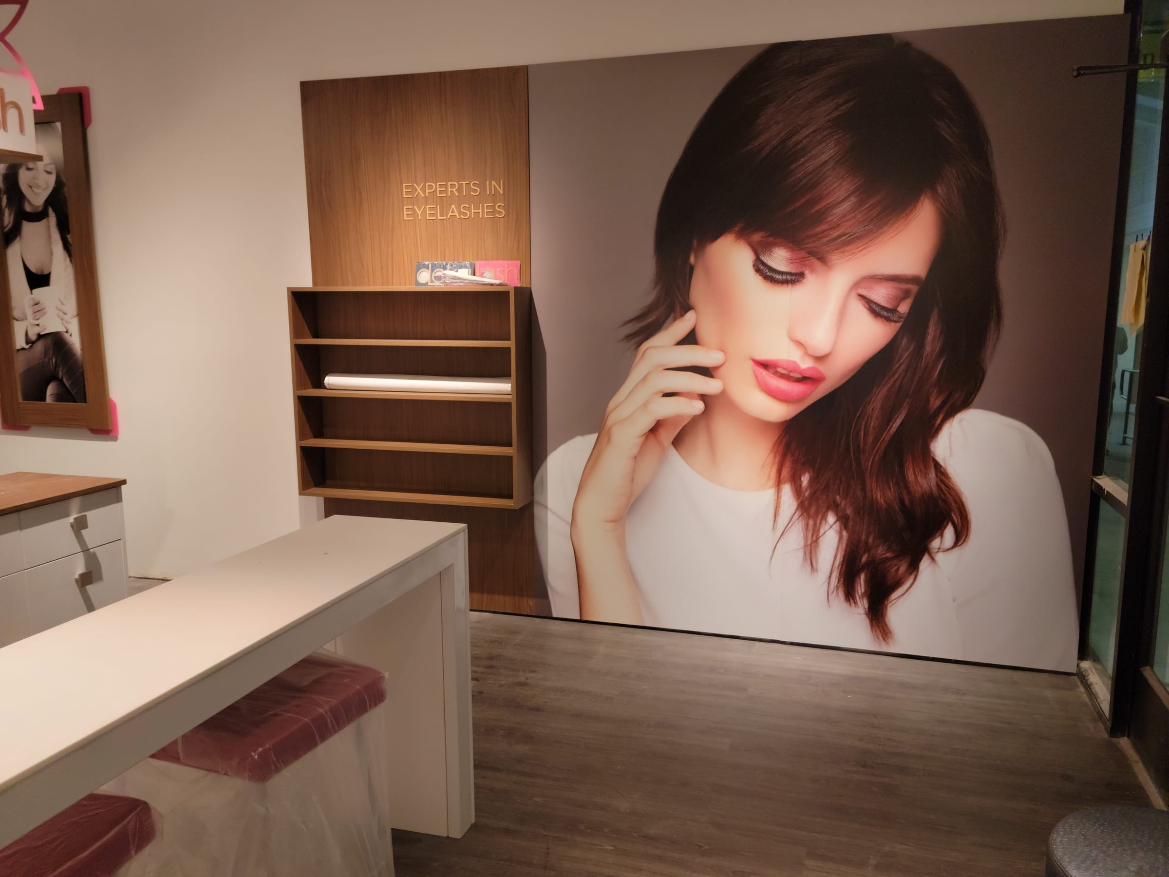 Experts in Eyelashes wall graphic and reception desk with wood shelving and new flooring