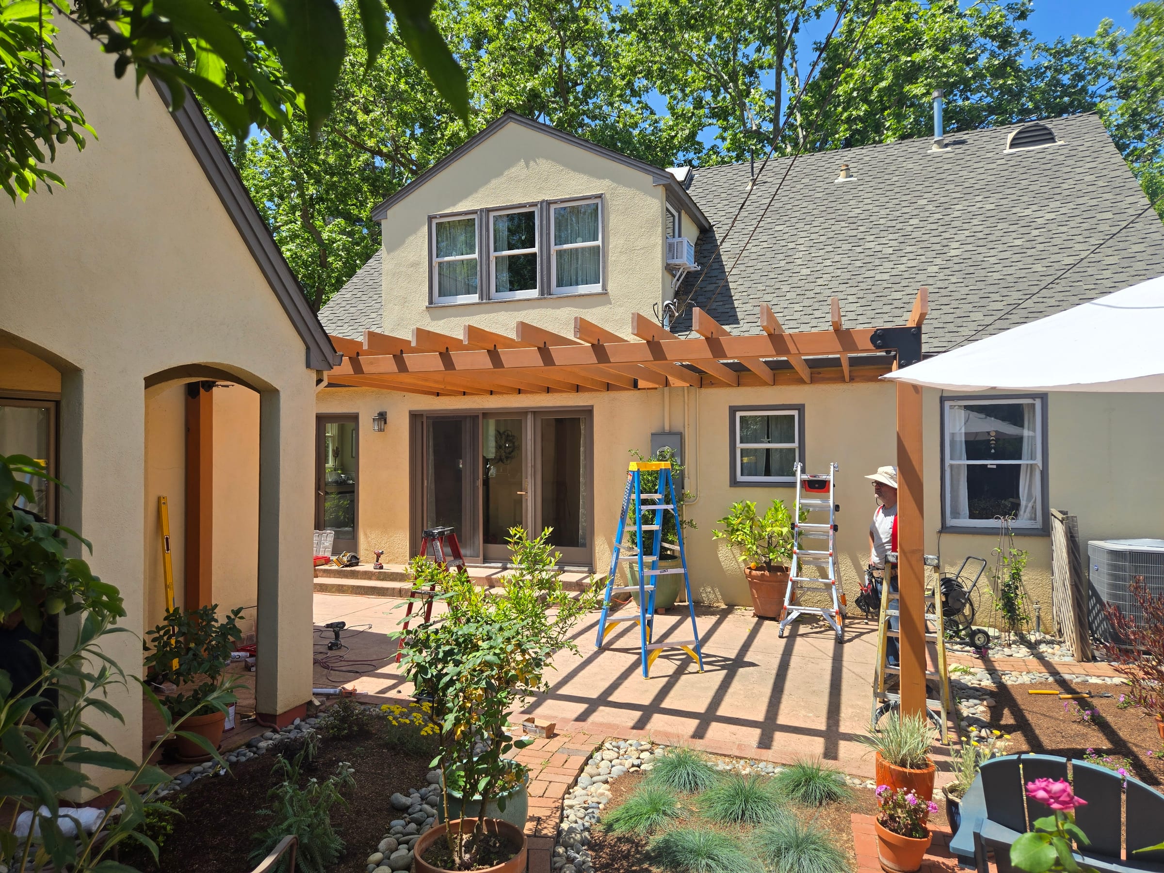 Pergola framing installed over the patio, house dormer window behind