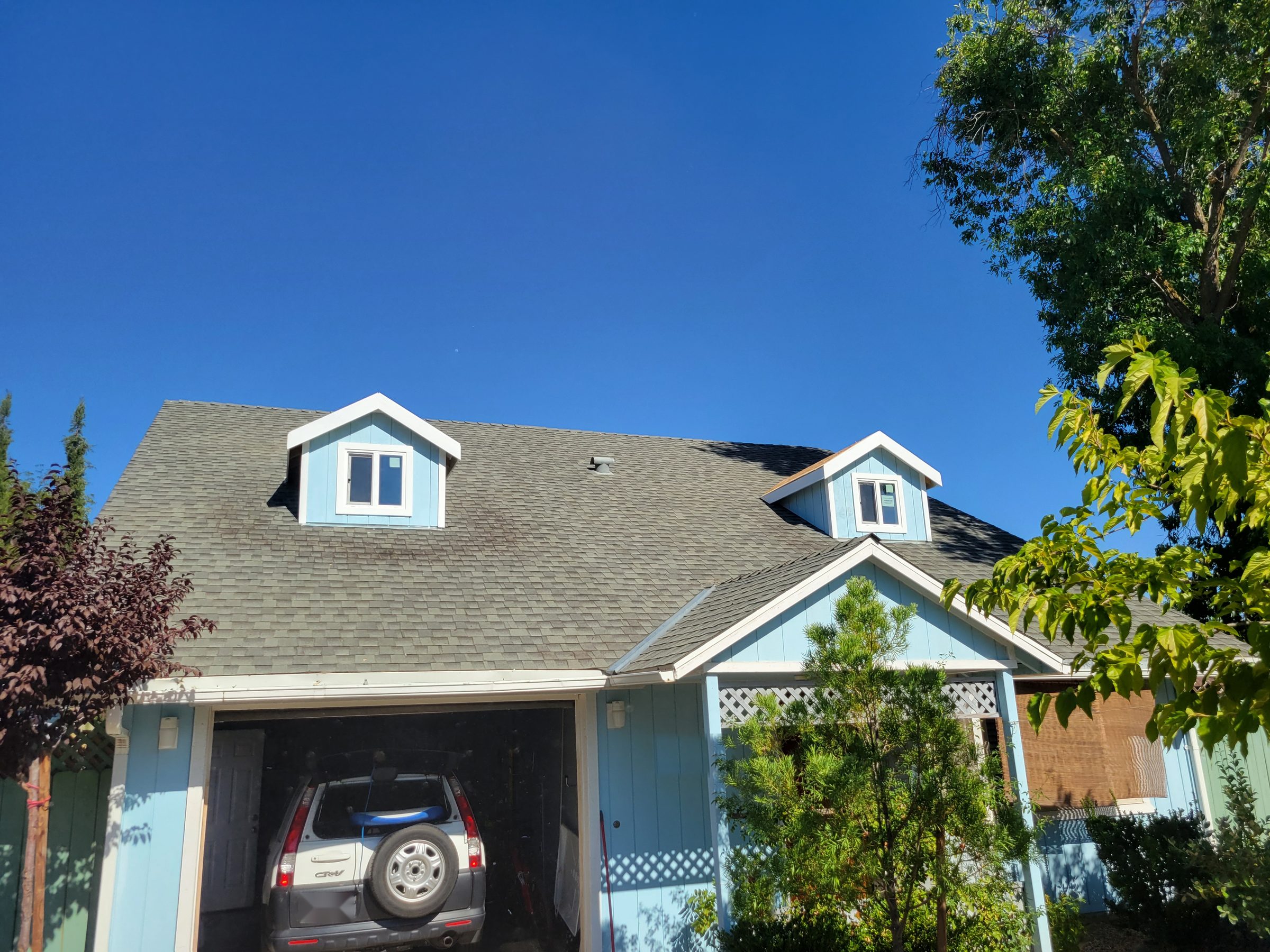 Two new dormers with white trim on a shingle roof above a garage entry