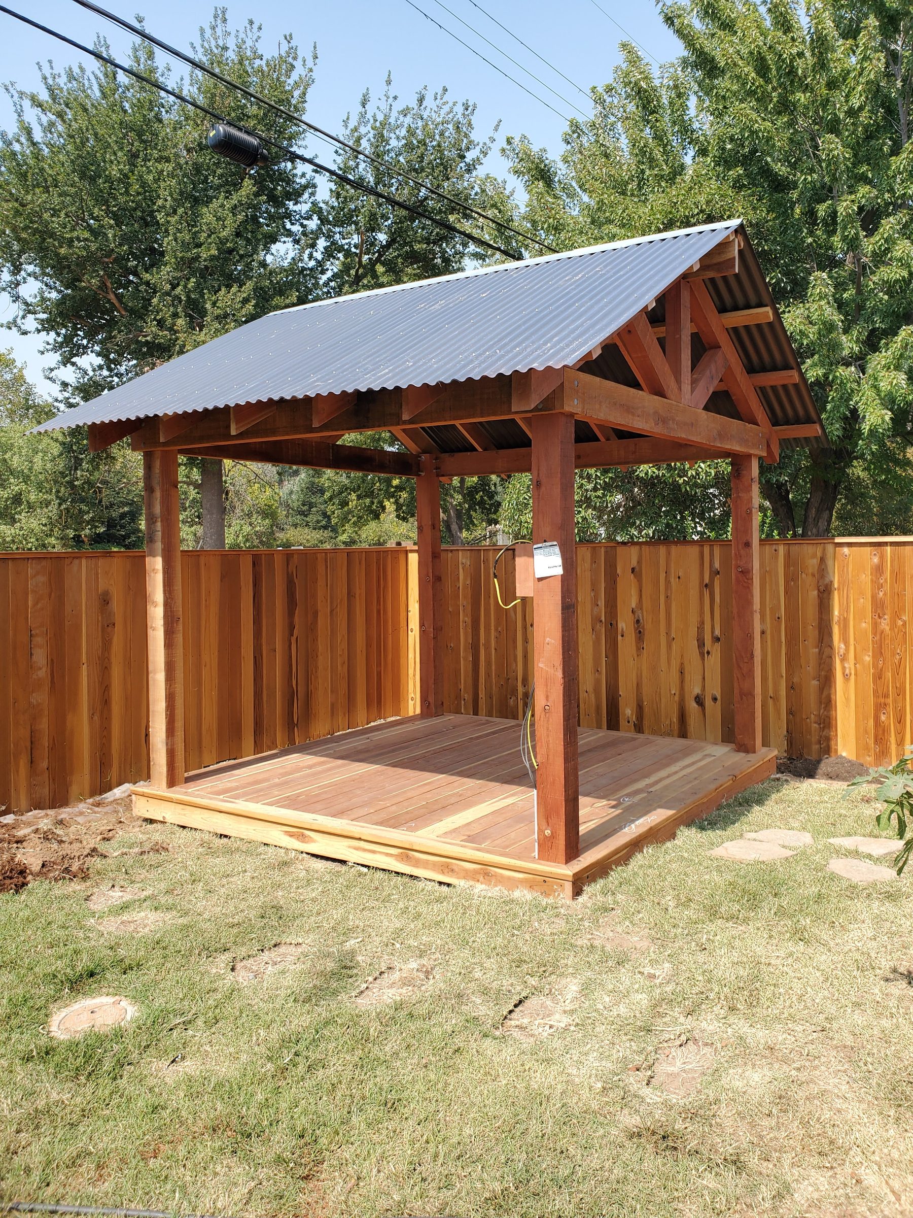 Newly built cedar gazebo with corrugated metal gable roof and raised wood deck floor