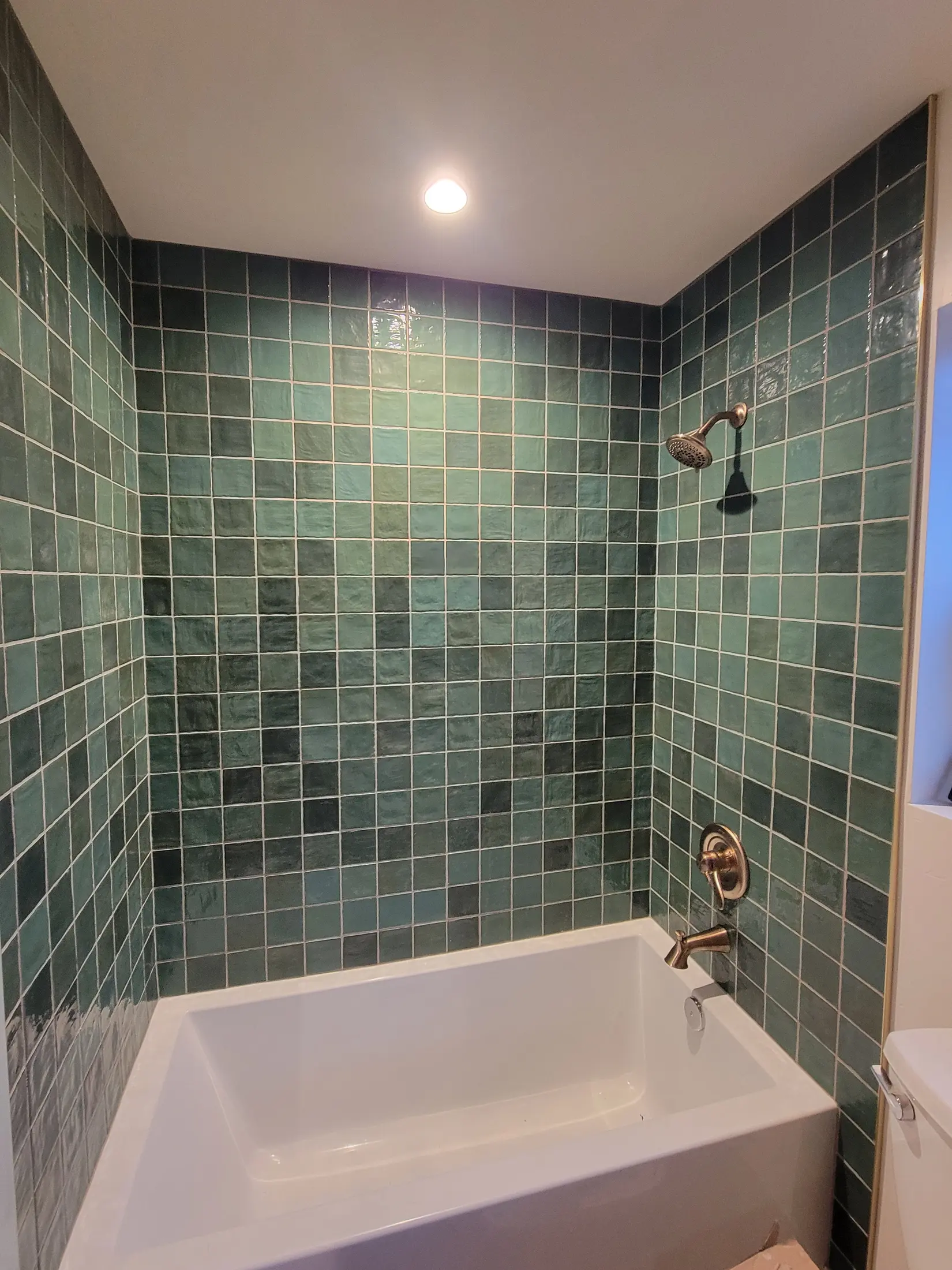 Second finished view of the green tiled bath and warm metal fixtures