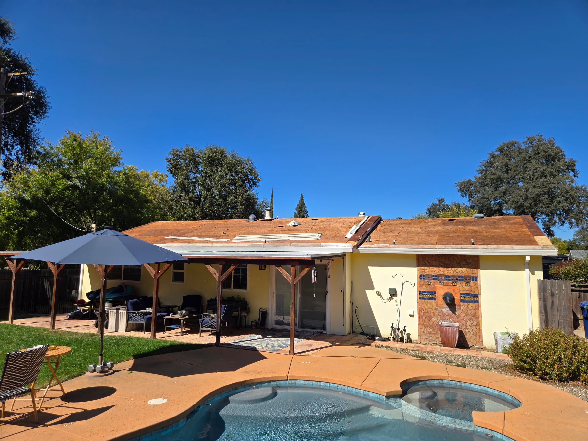 Roof torn down to bare wood sheathing over a backyard patio and pool before reroofing