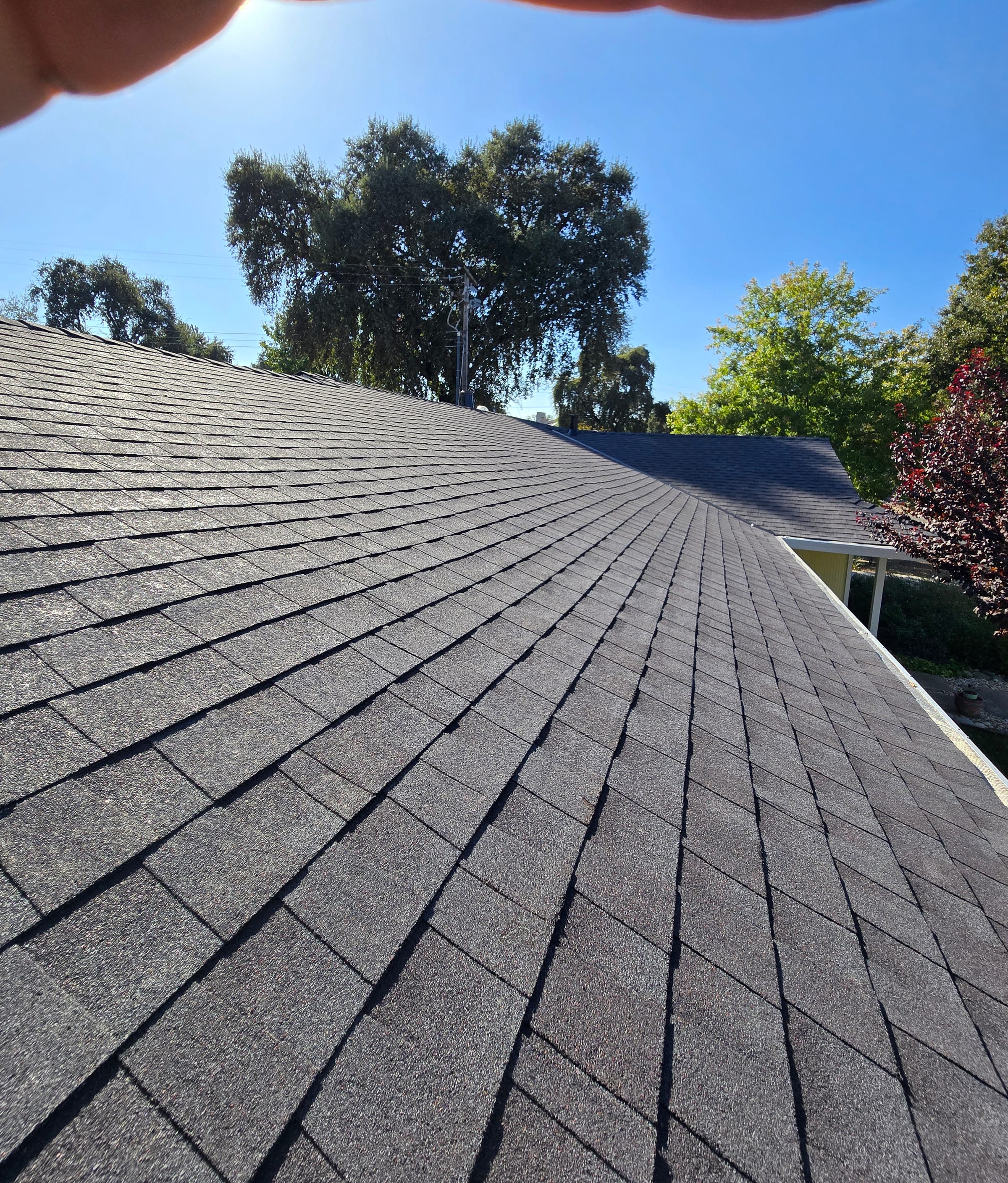 Close-up looking down the finished shingle roofline from the ridge to the eave