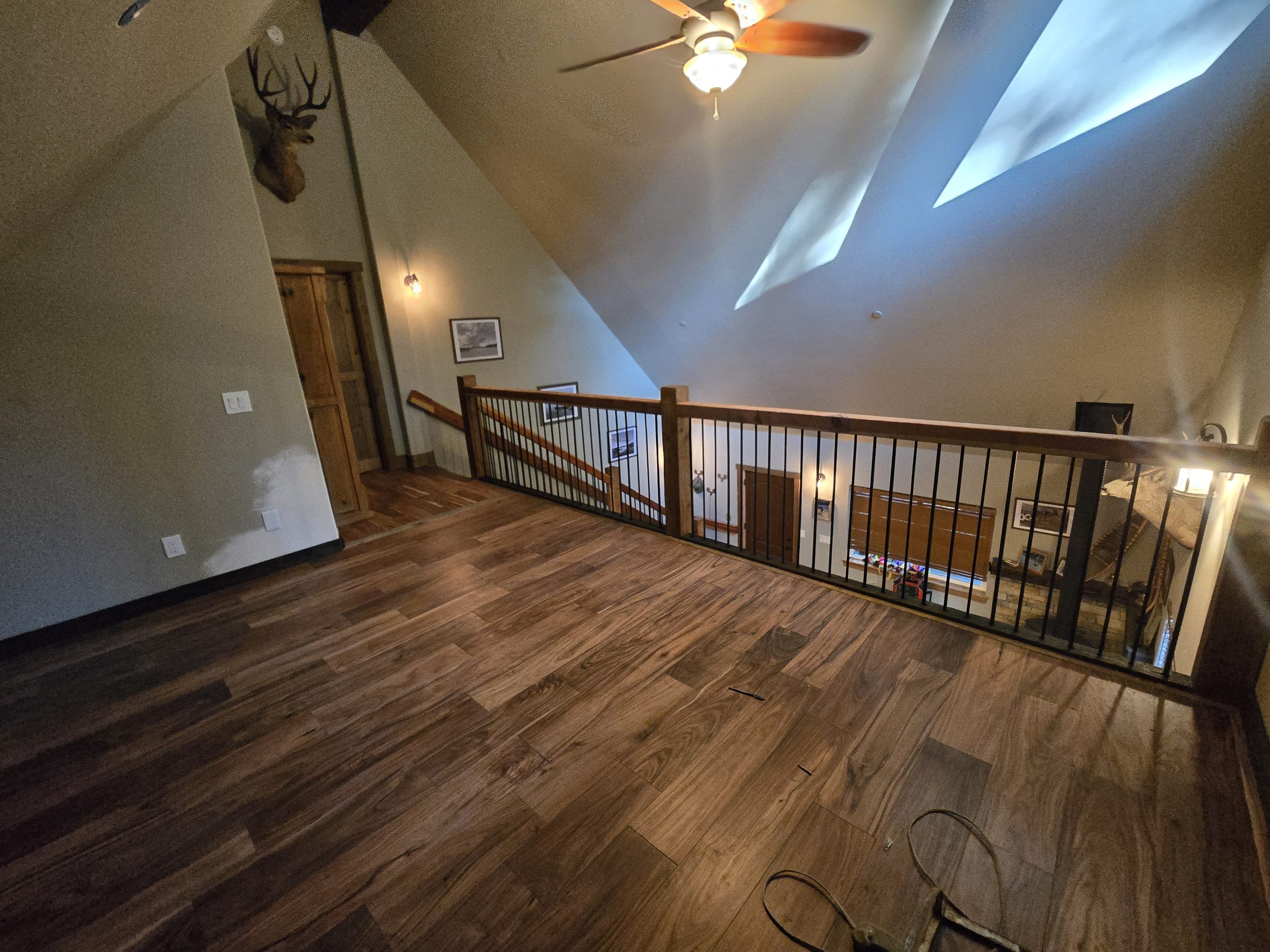 Wide view of a loft with hardwood flooring, iron railing and skylights