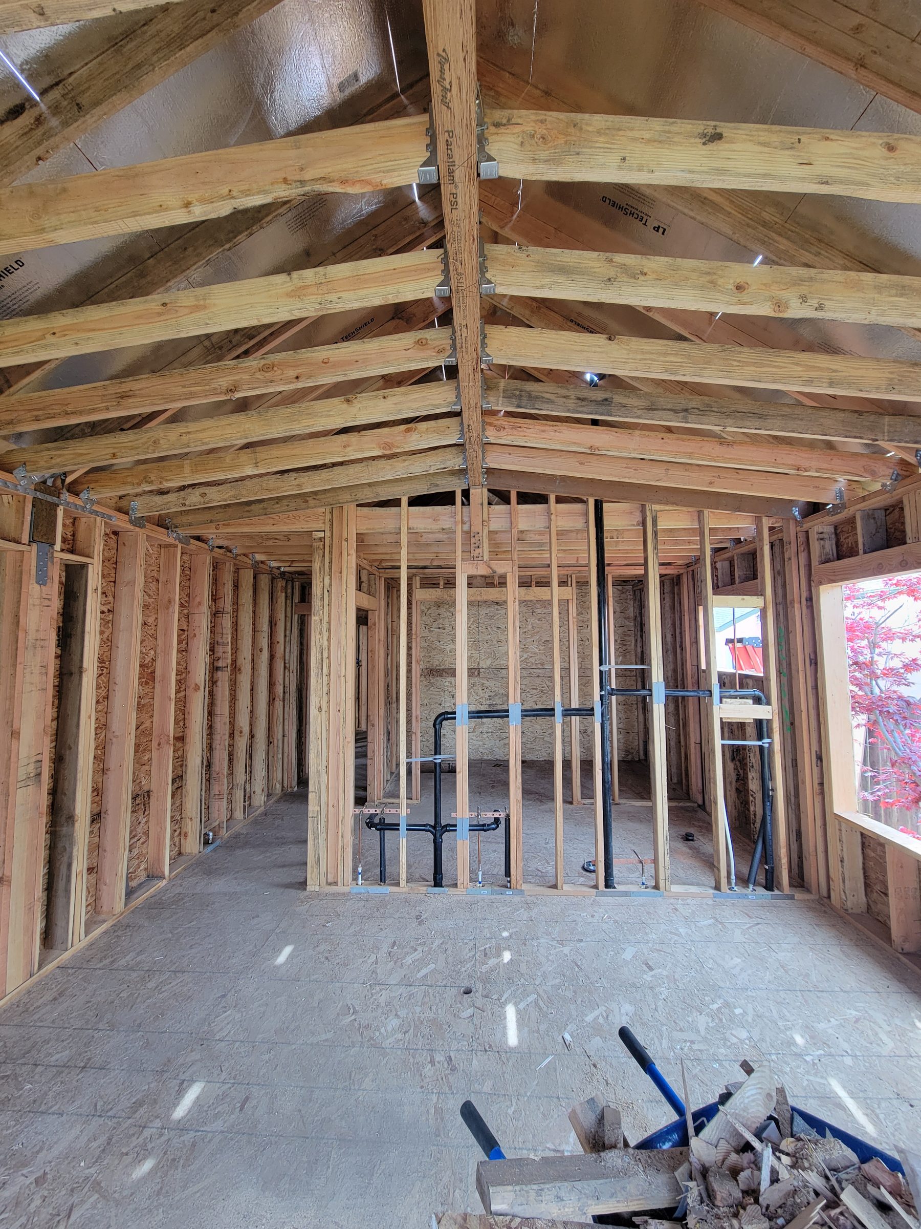 Interior of a framed addition with vaulted roof framing and rough plumbing