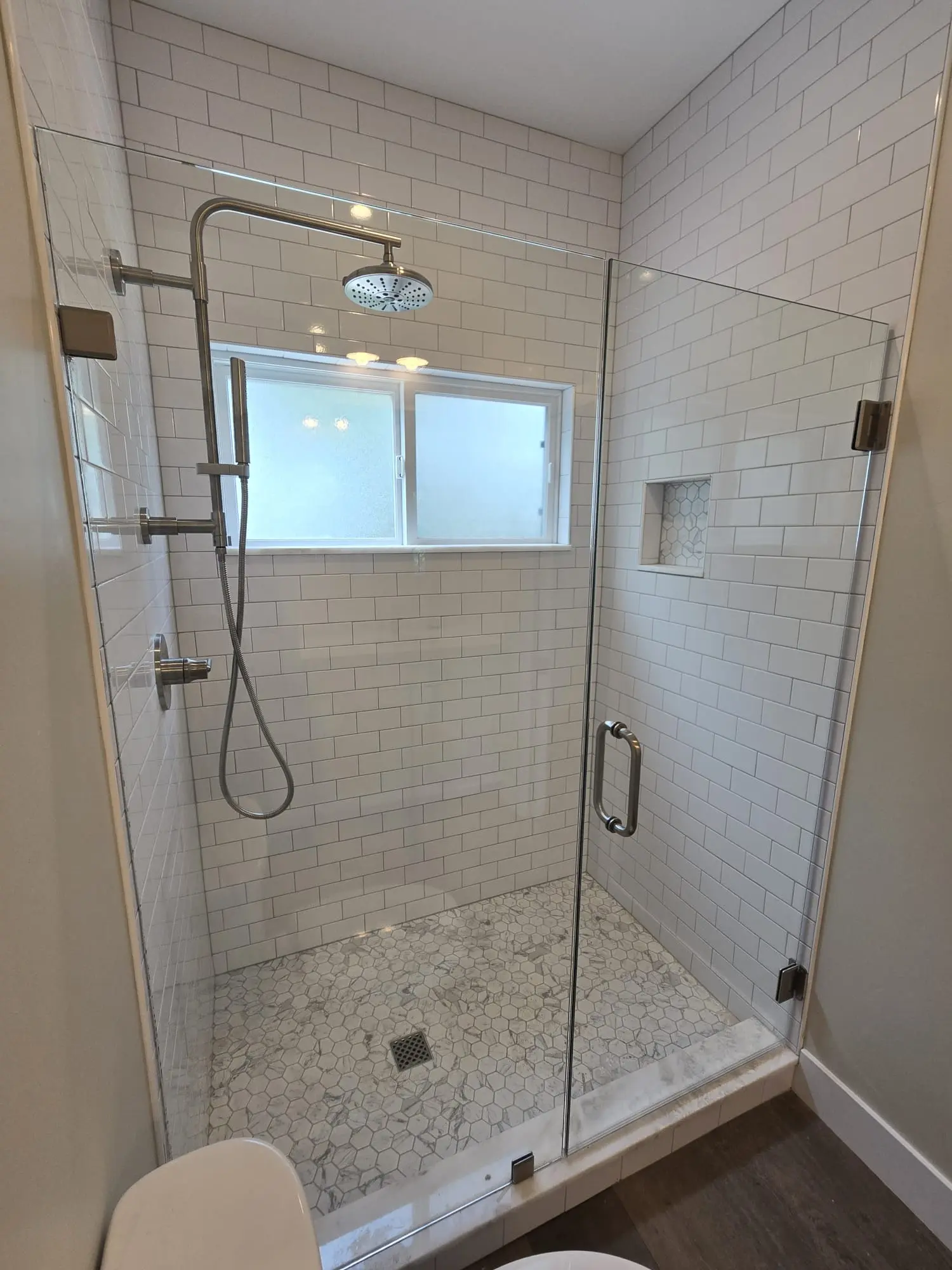 Finished ADU shower with white tile, glass enclosure, and built-in niche