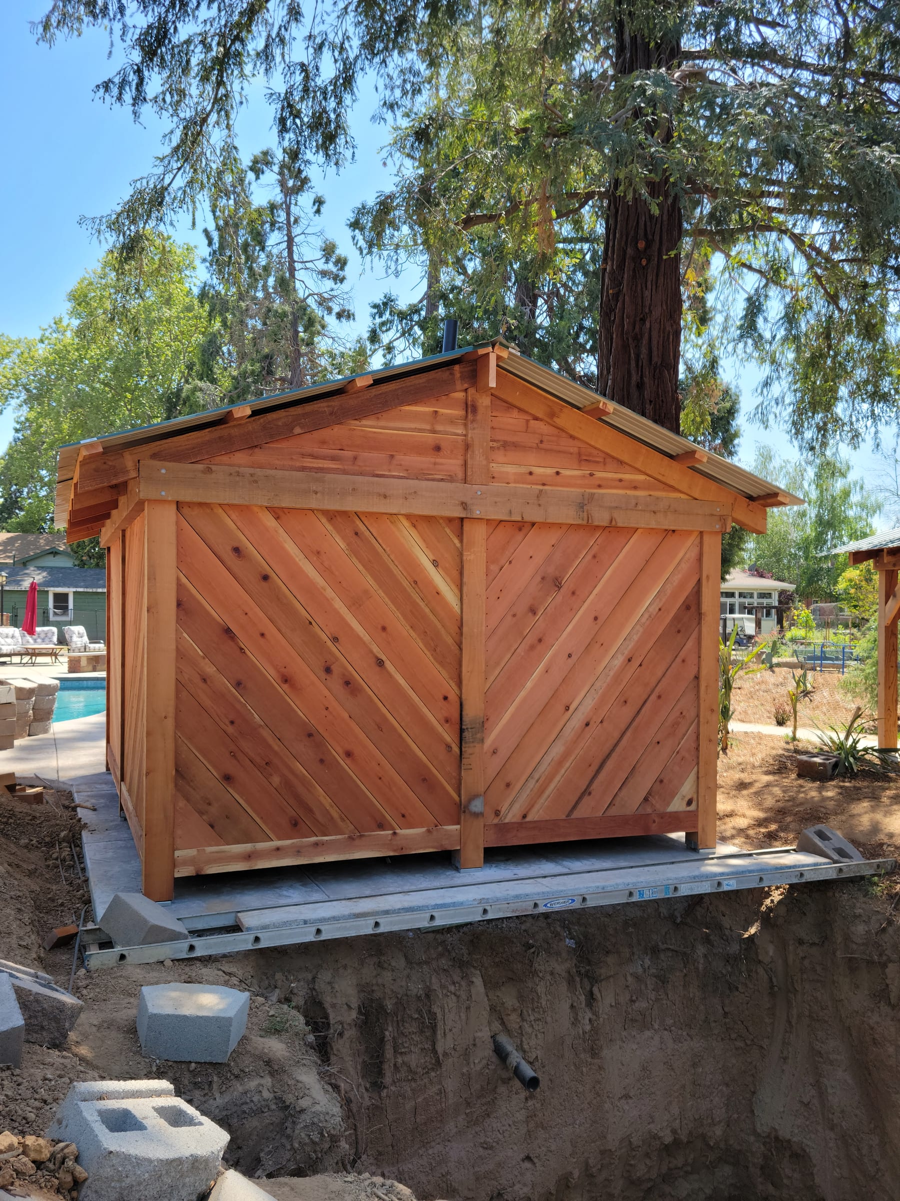 Cedar pool bathroom structure with green metal roof, backyard pool visible alongside