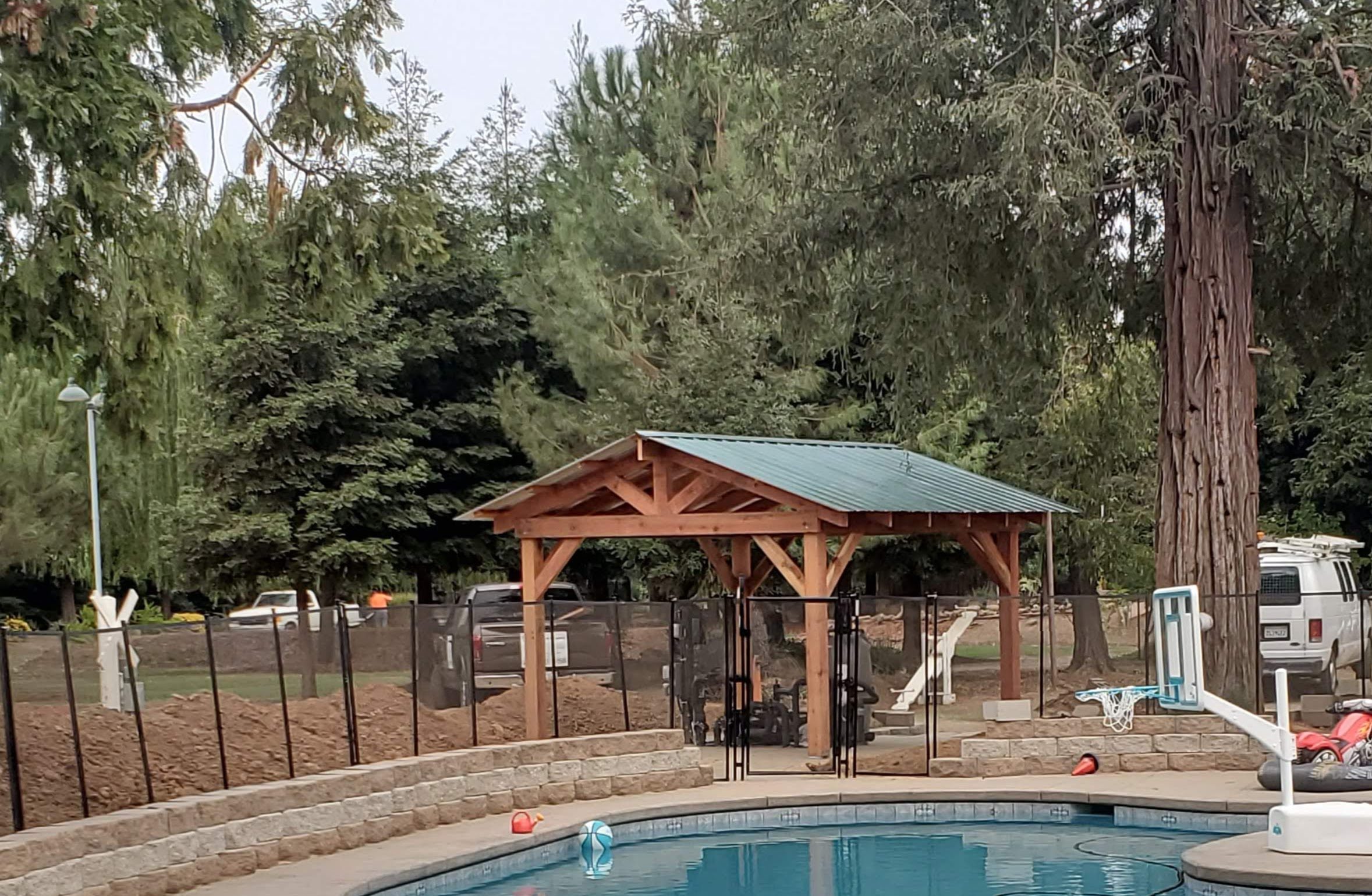 Timber-framed gazebo with green metal roof beside a backyard pool