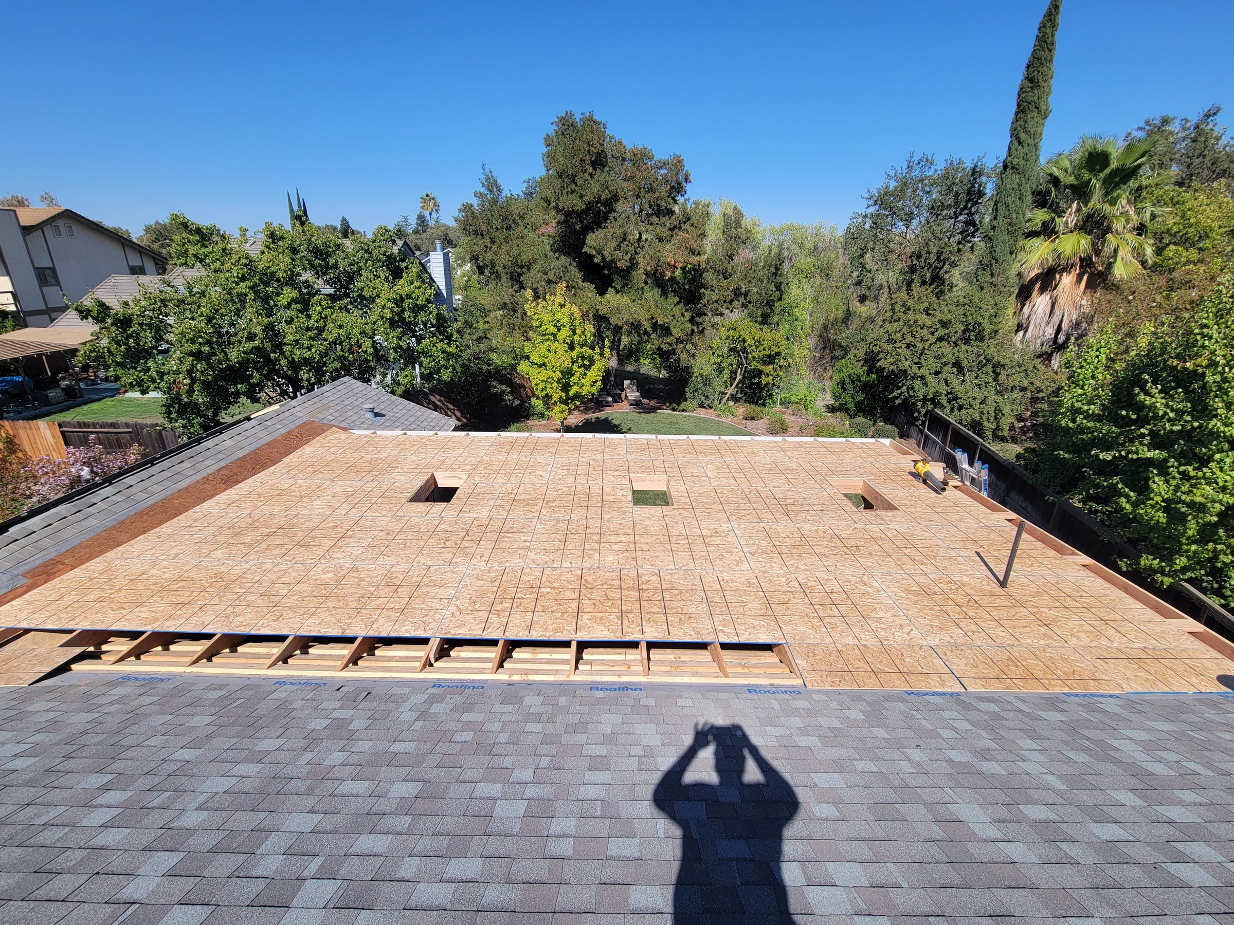 Roof deck sheathing installed over new framing next to an existing shingle roof