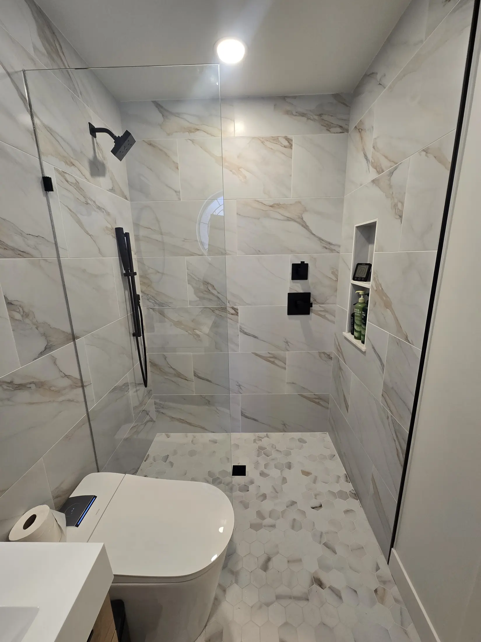 Finished marble-look wet room with glass partition and black fixtures