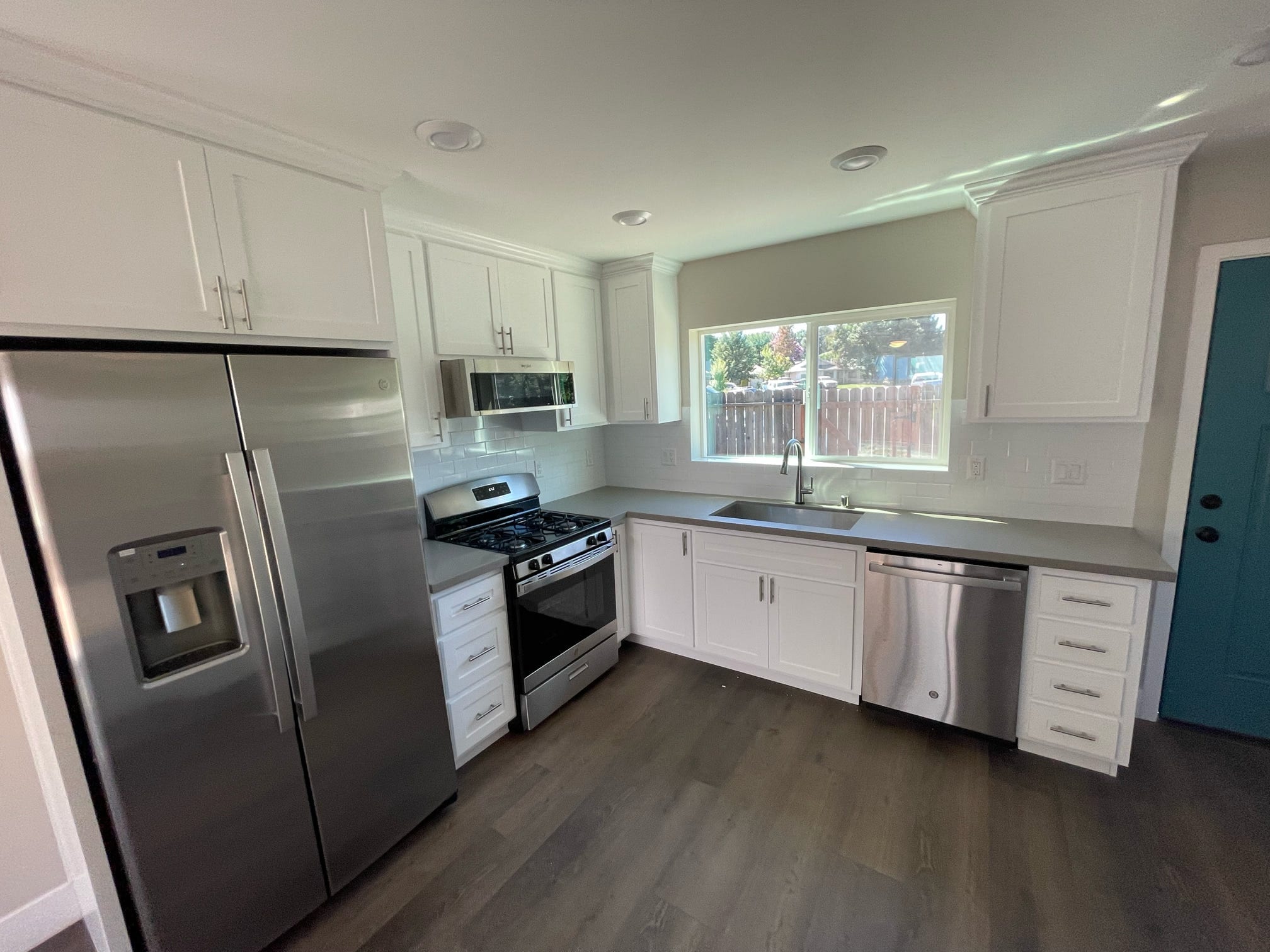White kitchen with gray countertops, subway tile backsplash, and stainless appliances